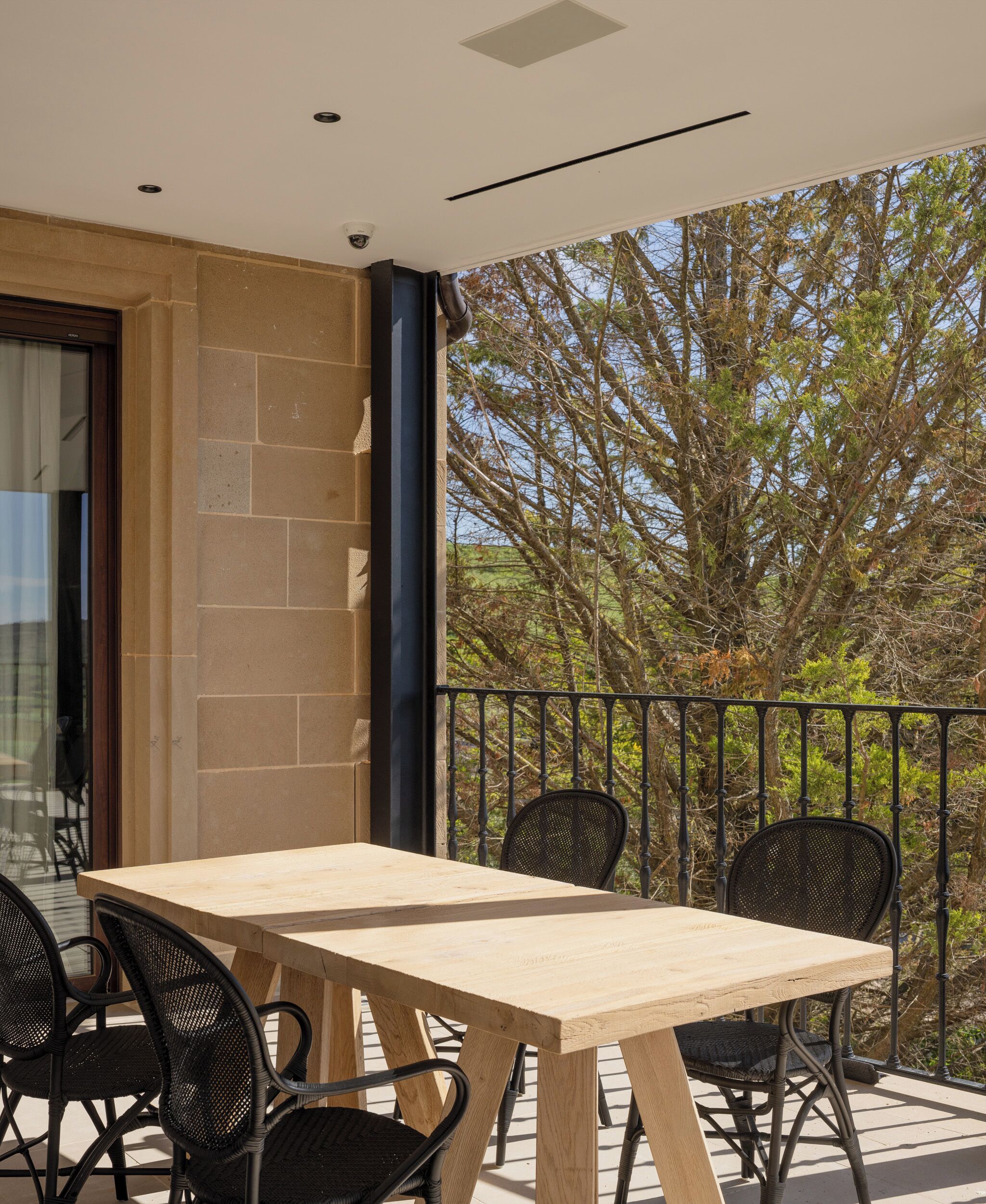 Ein Balkon mit Holztisch und vier Stühlen, eine Steinmauer und Blick auf Bäume.