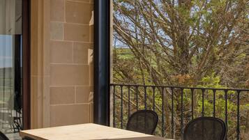 Ein Balkon mit Holztisch und vier Stühlen, eine Steinmauer und Blick auf Bäume.