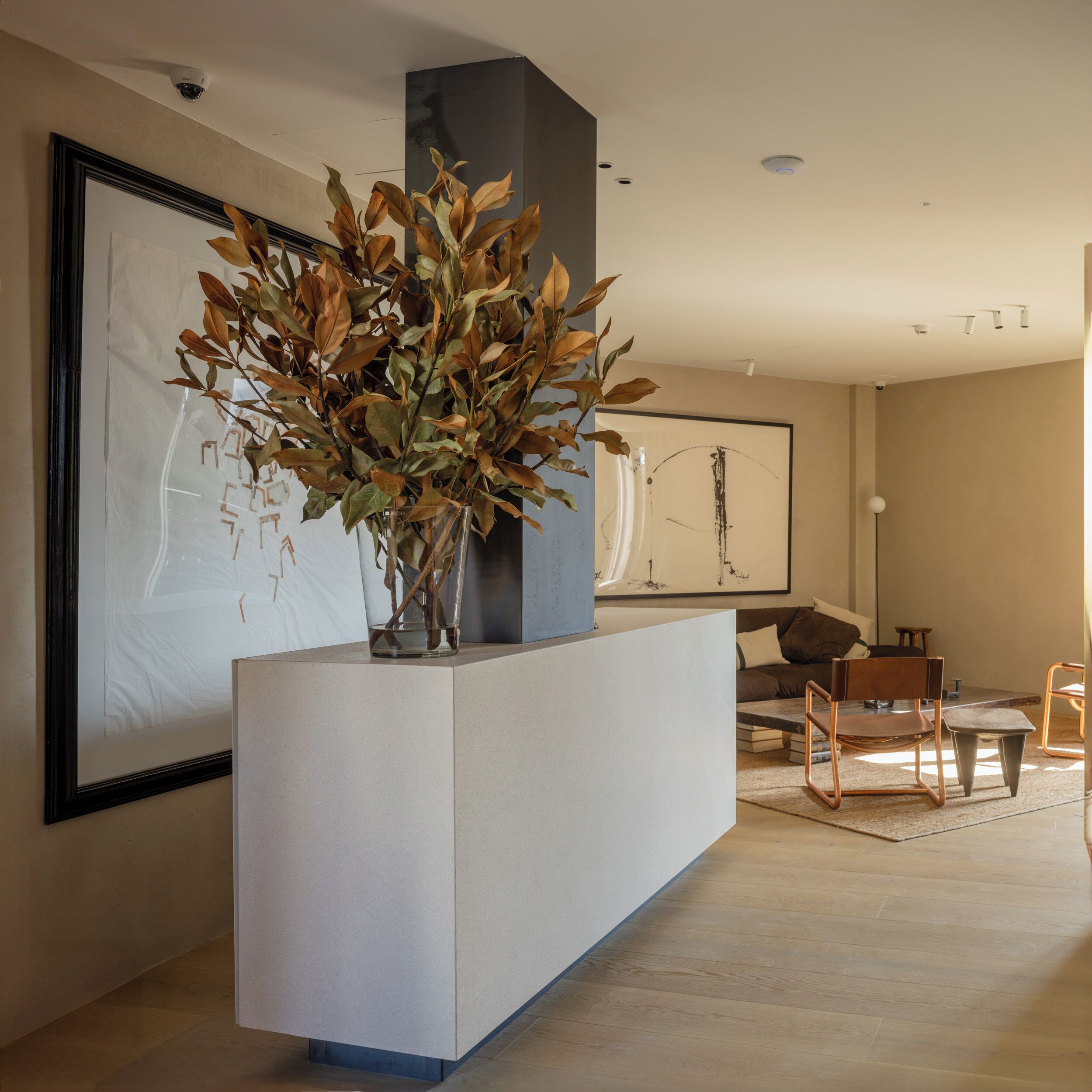 A modern reception area with a white reception desk, a large framed abstract painting, and a potted plant with dried leaves.