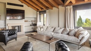 A spacious living room with a large sofa, a fireplace, a TV, and a view of the outdoors. - Hotel Boutique Mirador de Deyo (Villamayor de Monjardín)