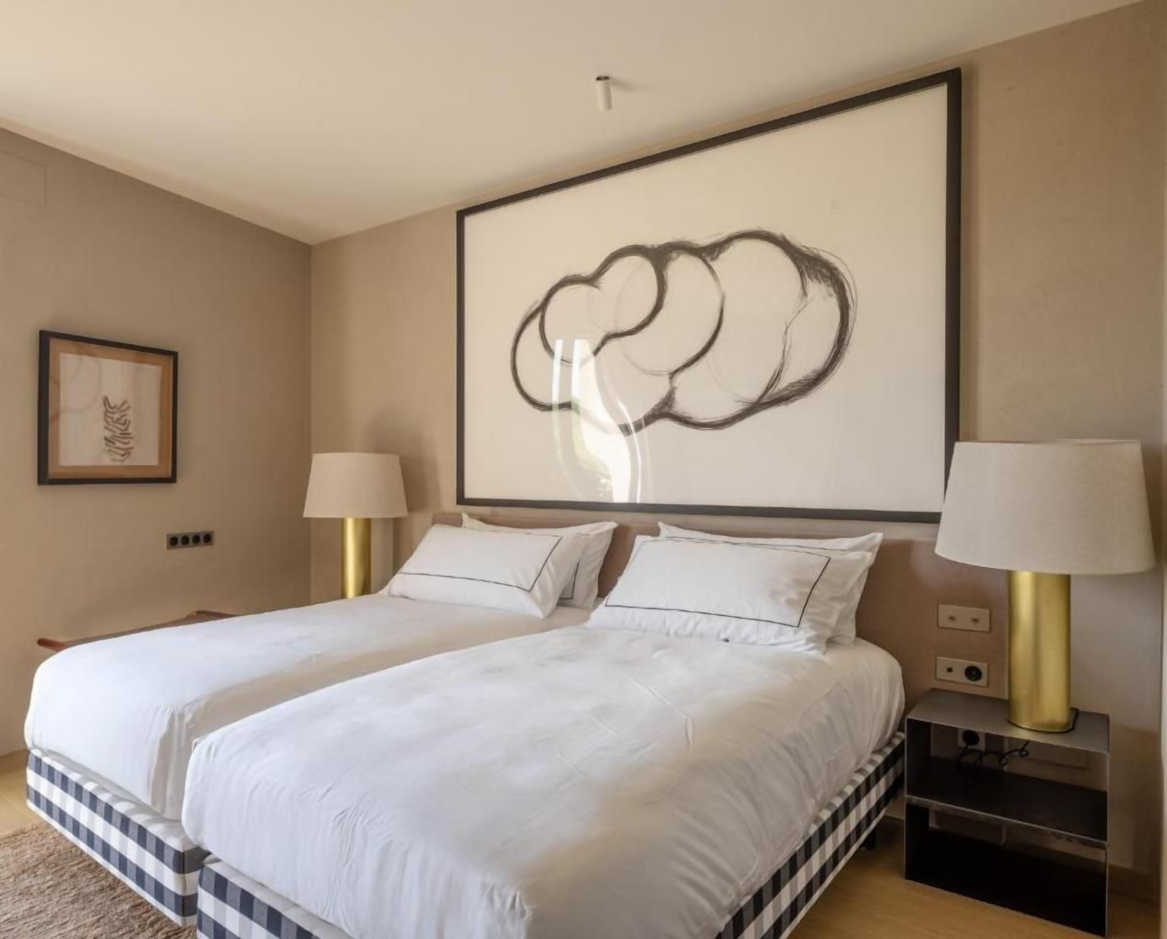 A hotel room with a large bed, two bedside tables, a wall-mounted artwork, and a framed picture on the wall.