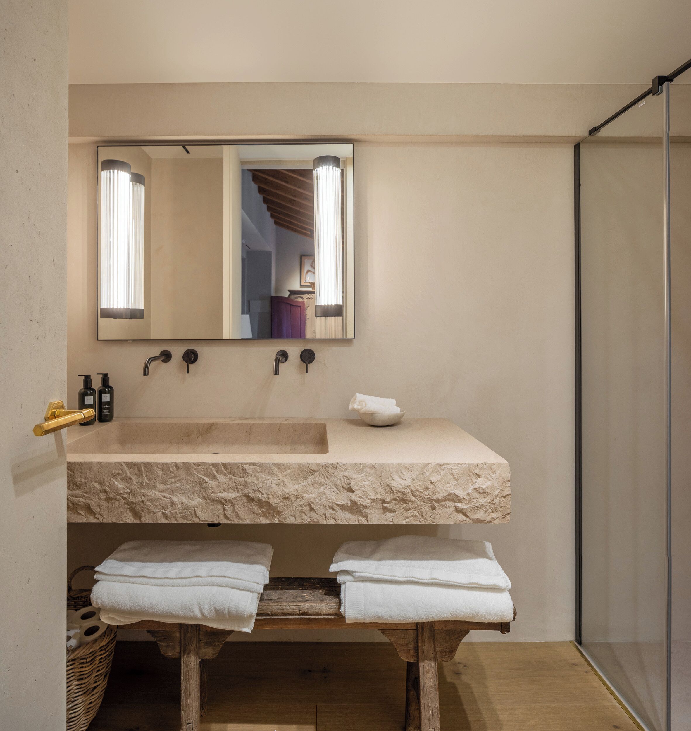 A bathroom with a stone sink, a mirror, and two towels on a wooden bench.