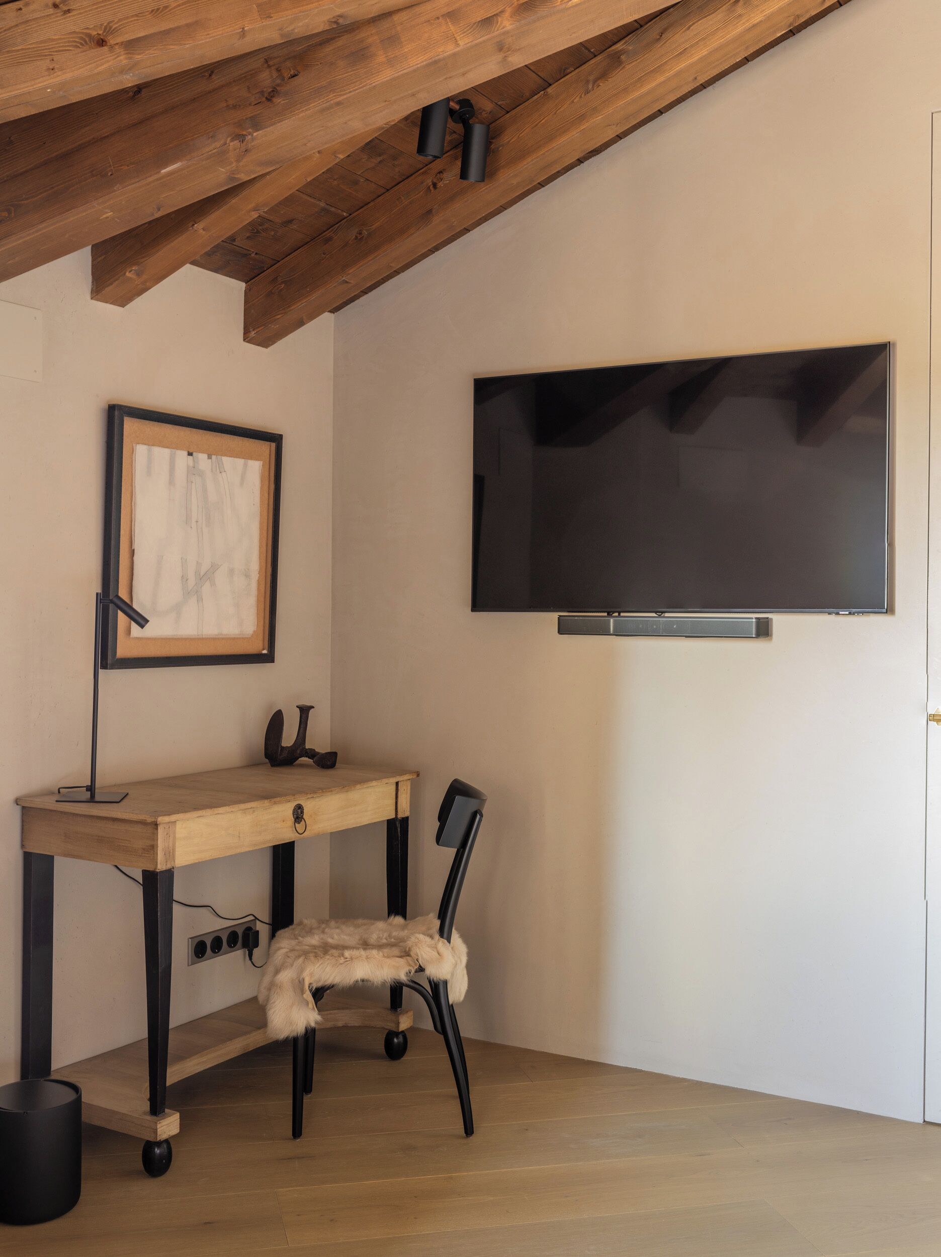 Une pièce comprenant un bureau en bois, une chaise, un tableau encadré et un téléviseur fixé au mur.