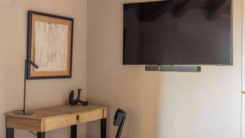Une pièce comprenant un bureau en bois, une chaise, un tableau encadré et un téléviseur fixé au mur.