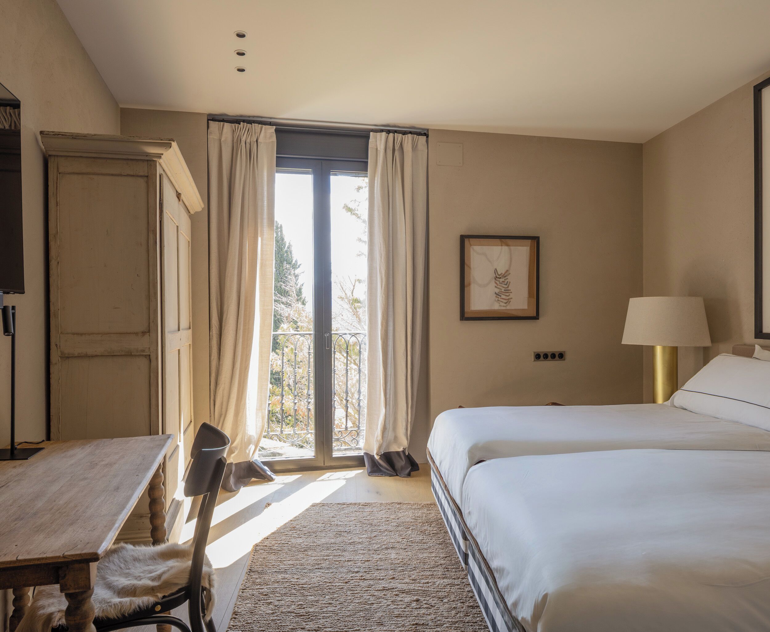 A bedroom with a bed, a desk, a chair, a lamp, and a window with curtains.