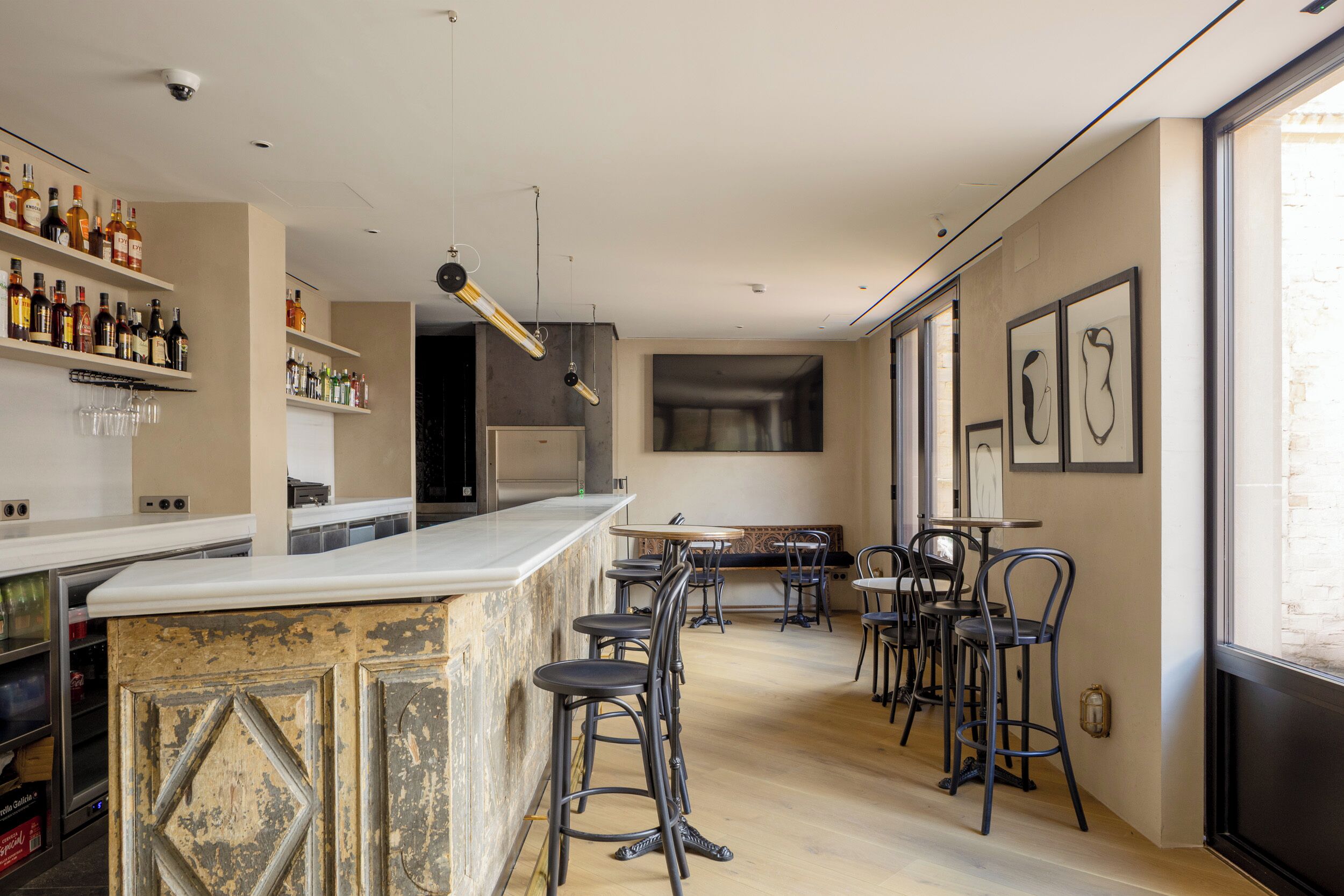 A bar area with a counter, stools, and shelves of bottles. There are tables and chairs in the background.