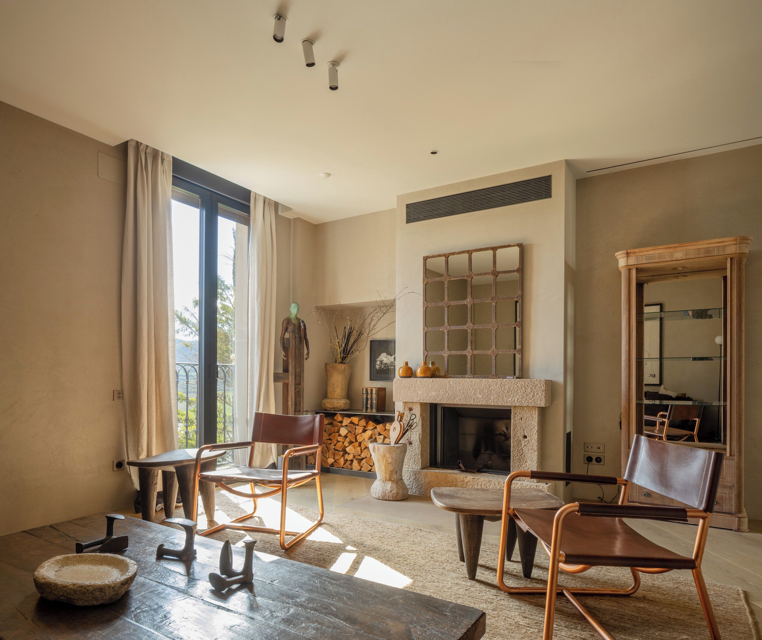 A living room with a fireplace, two leather chairs, a wooden table, and a large mirror.