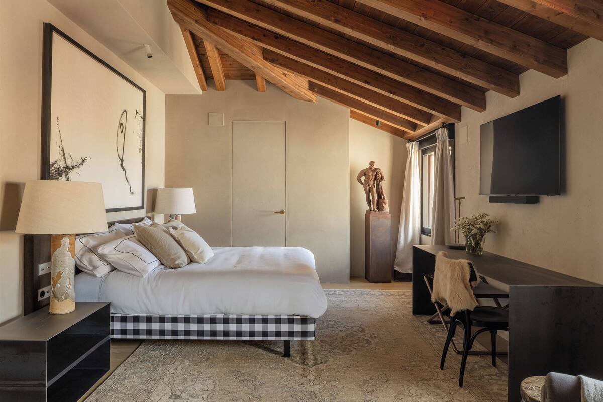 A bedroom with a bed, bedside tables, a desk, a chair, a television, and a statue.
