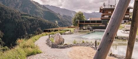 A mountain resort with a swimming pool, a wooden deck, and a view of the surrounding forest and mountains.