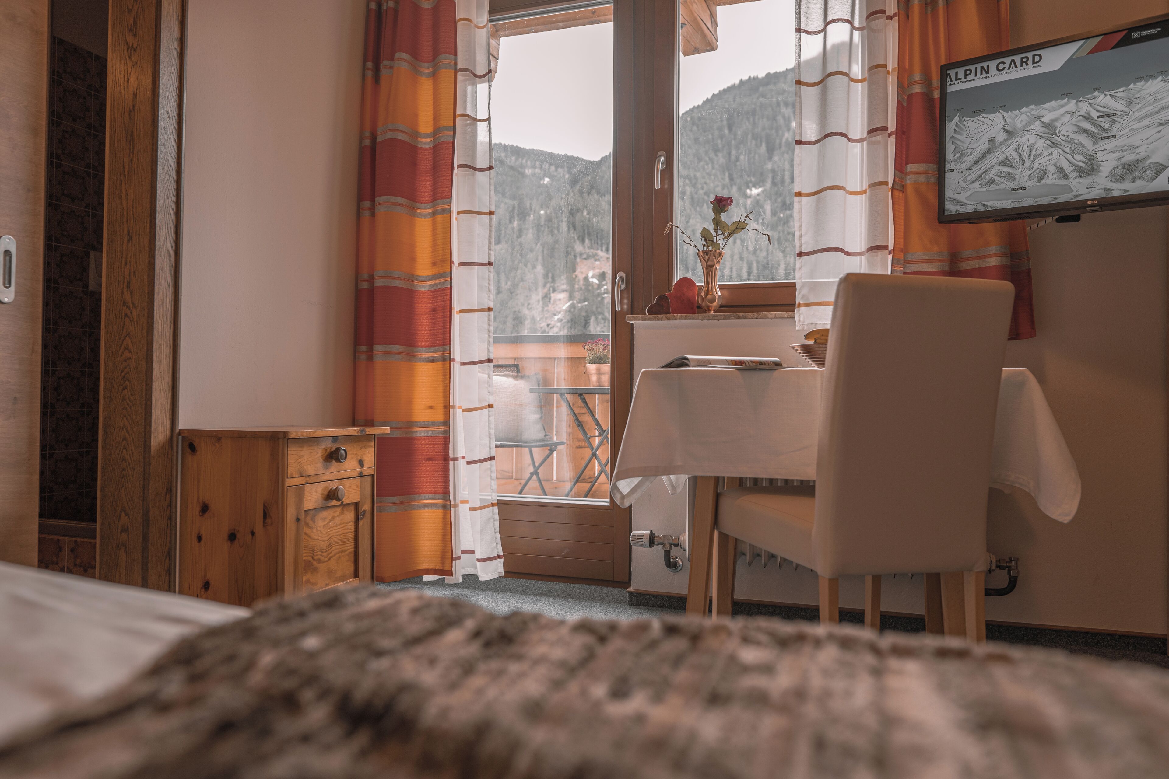 A hotel room with a bed, a desk with a chair, a television, and a window with curtains.