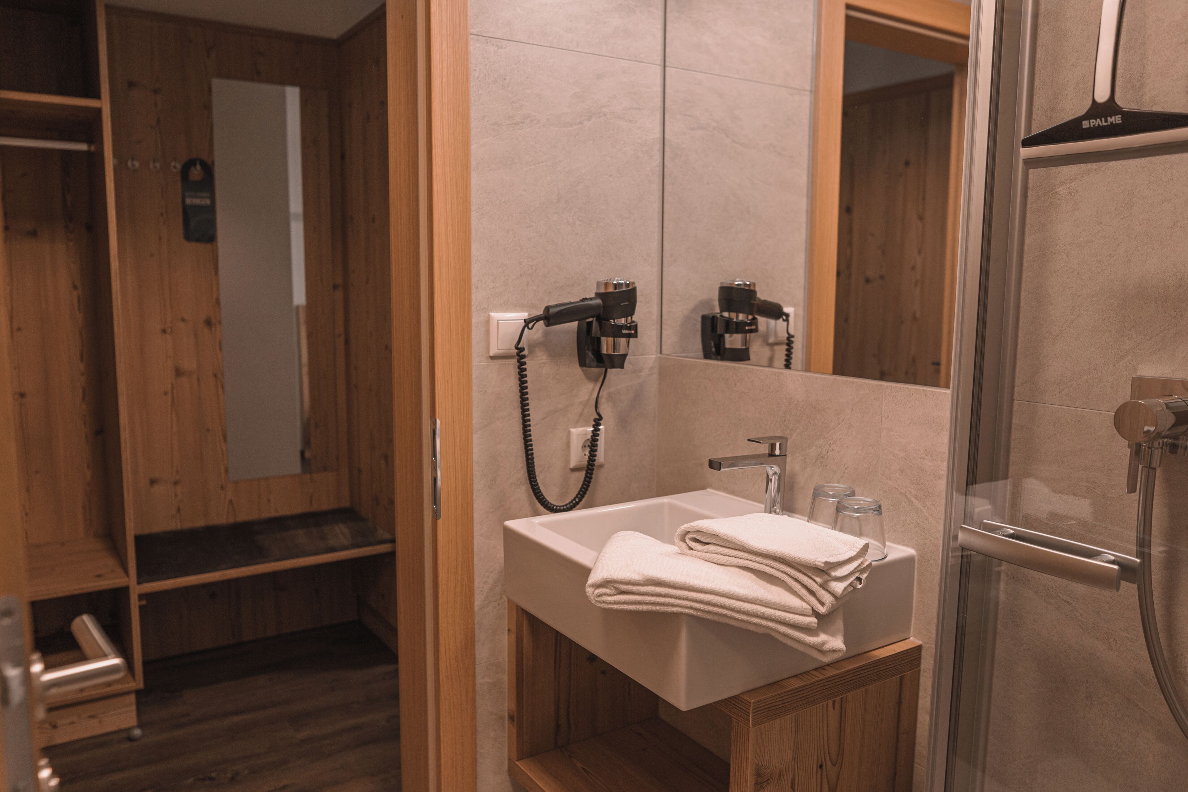 Un baño con tocador de madera, un lavamanos con toalla y zona de ducha.