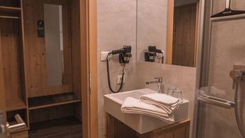 Un baño con tocador de madera, un lavamanos con toalla y zona de ducha.
