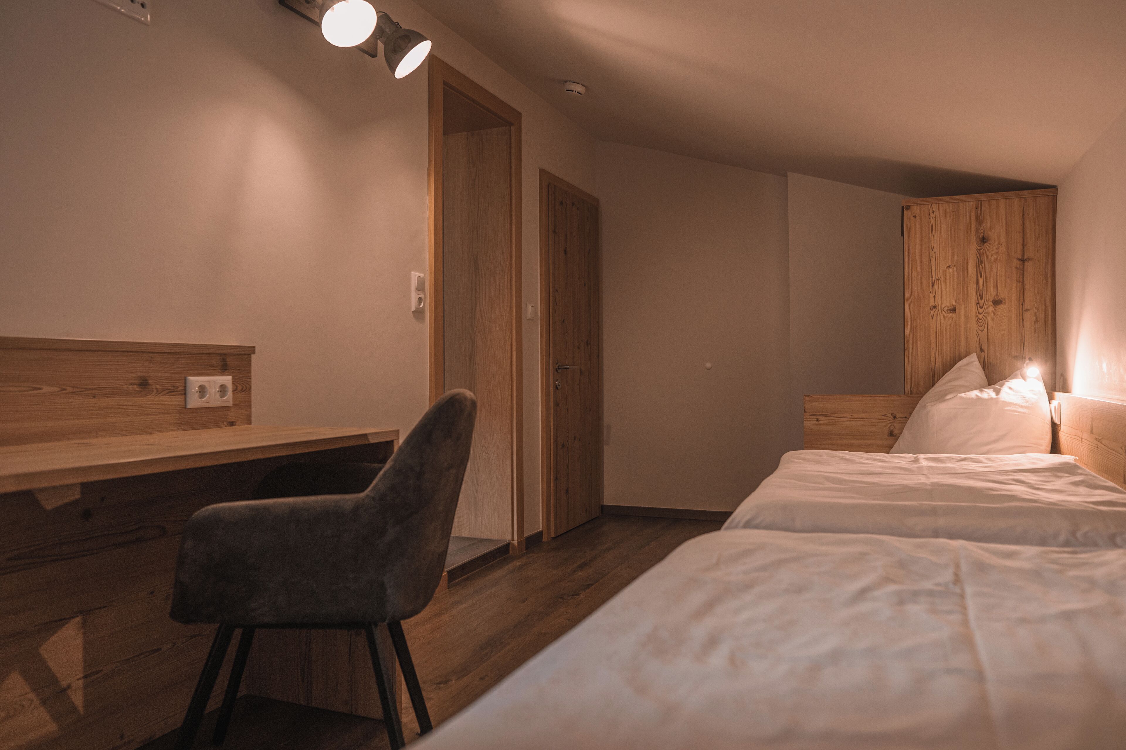 Ein Zimmer mit einem Holztisch, zwei Betten und einem Sessel.