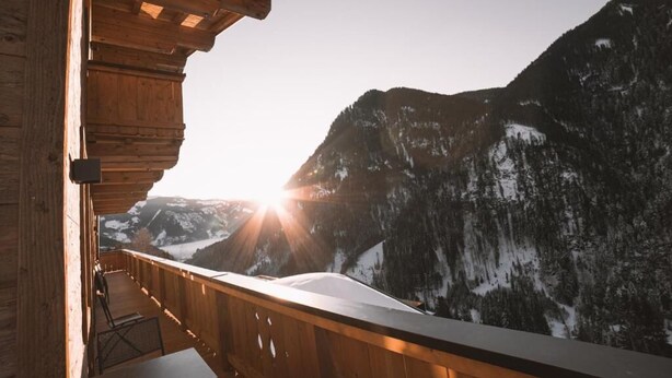 Ein Holzbalkon mit Blick auf schneebedeckte Berge und einen Sonnenauf- oder -untergang.