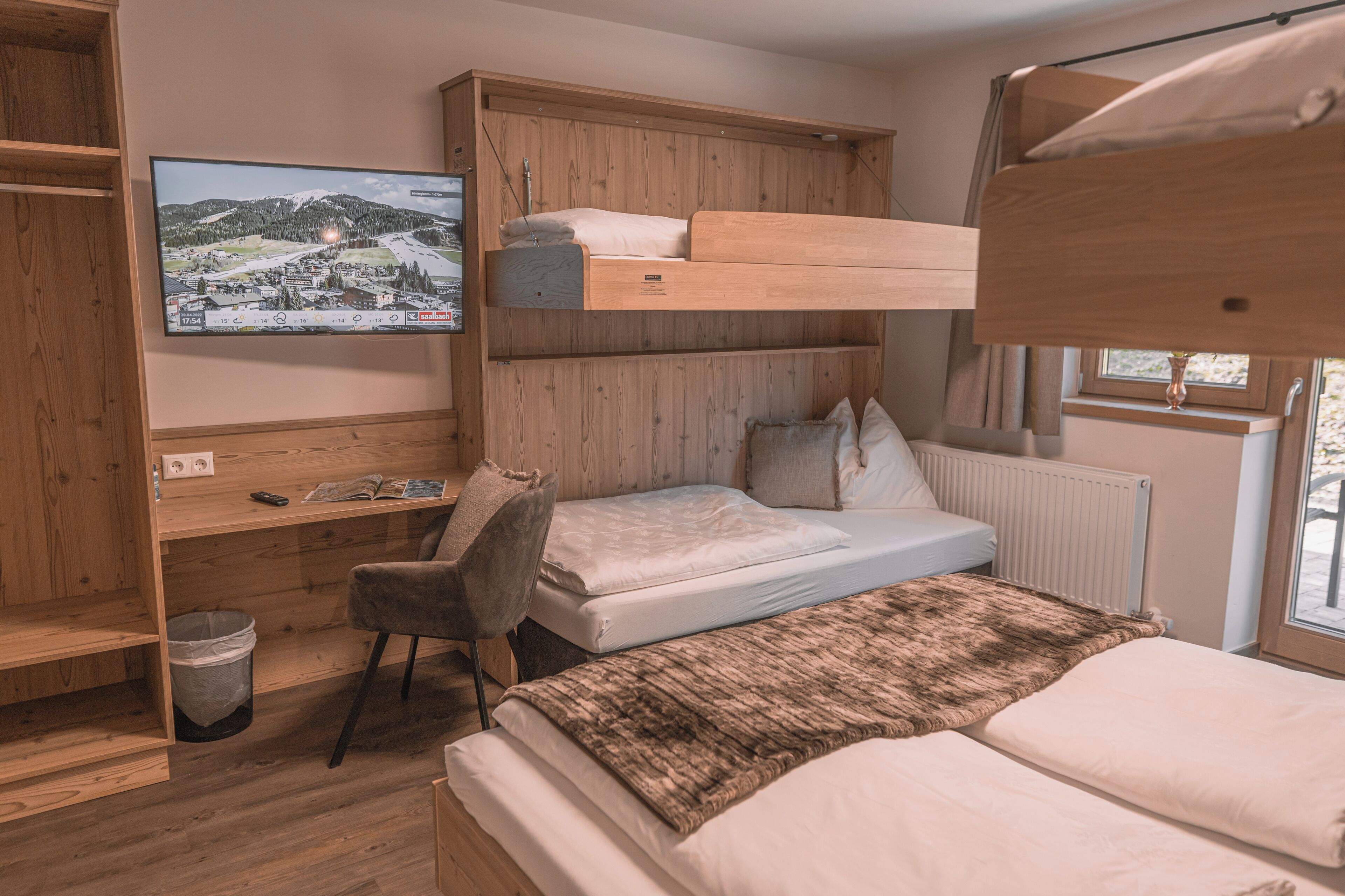 Ein kleines Zimmer mit Etagenbett, Schreibtisch, Stuhl und einem an der Wand befestigten Fernseher.