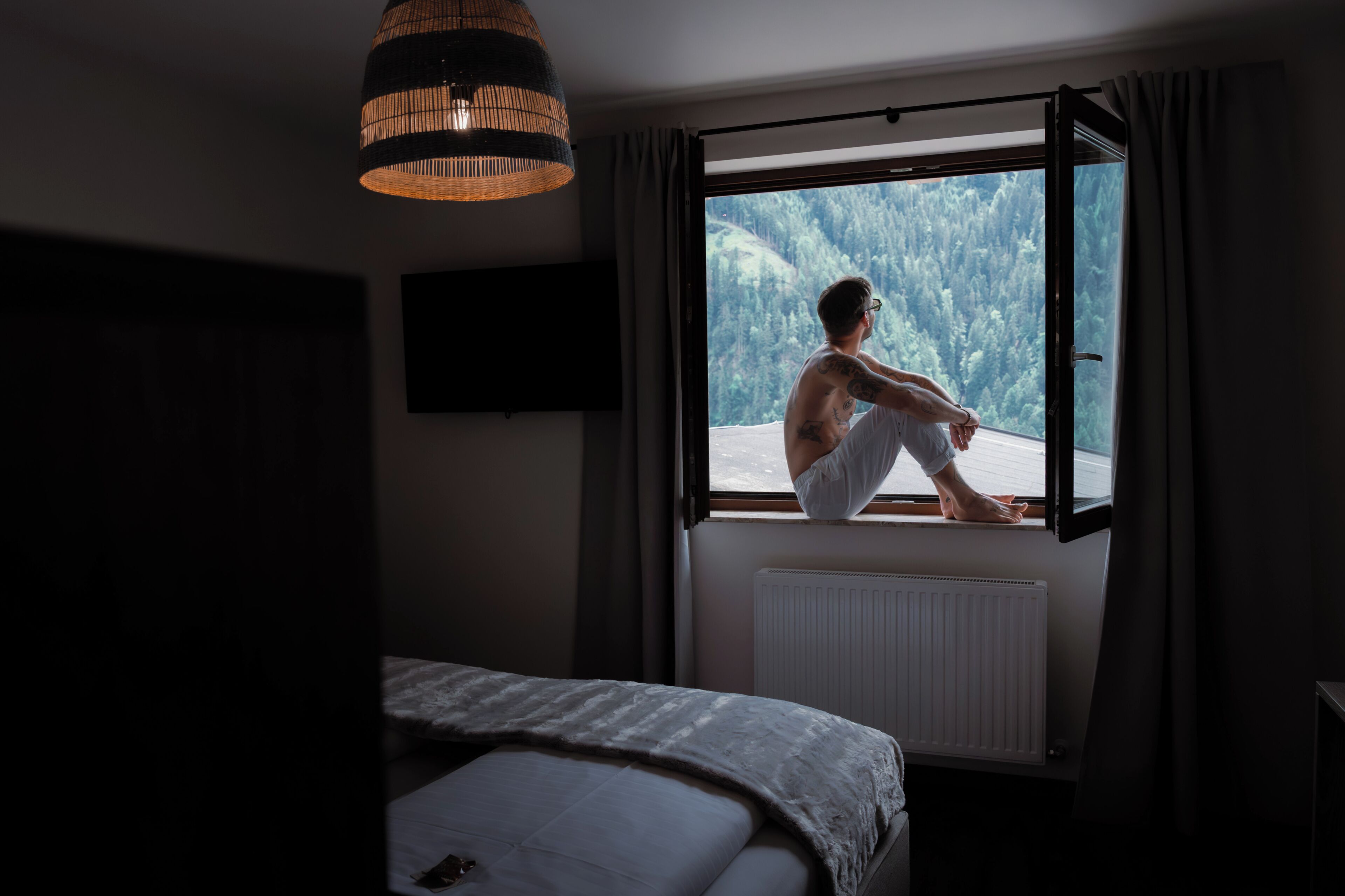 Una habitación con cama, ventana, radiador y lámpara colgante.