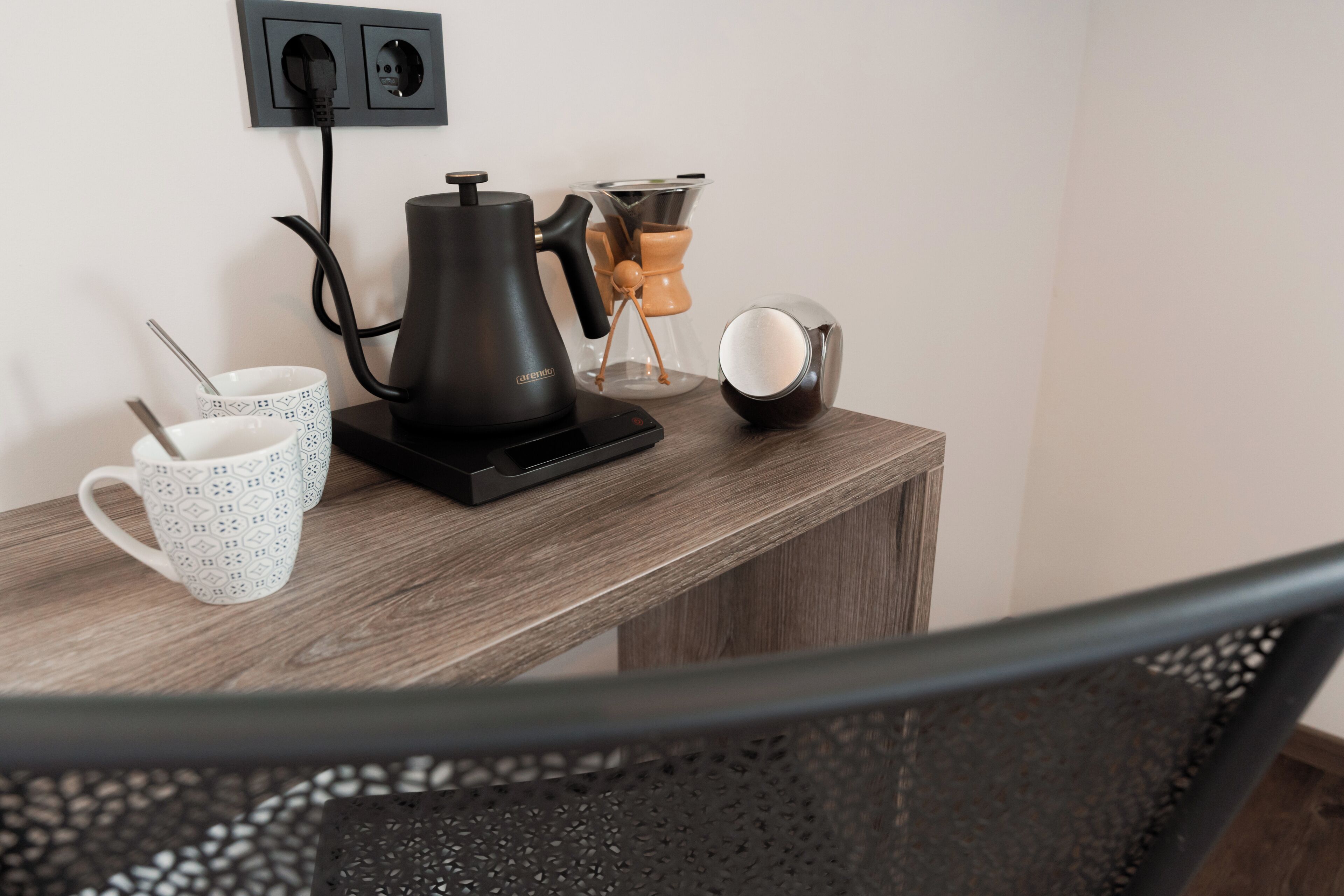 A coffee maker, a coffee pot, and a cup on a wooden table.
