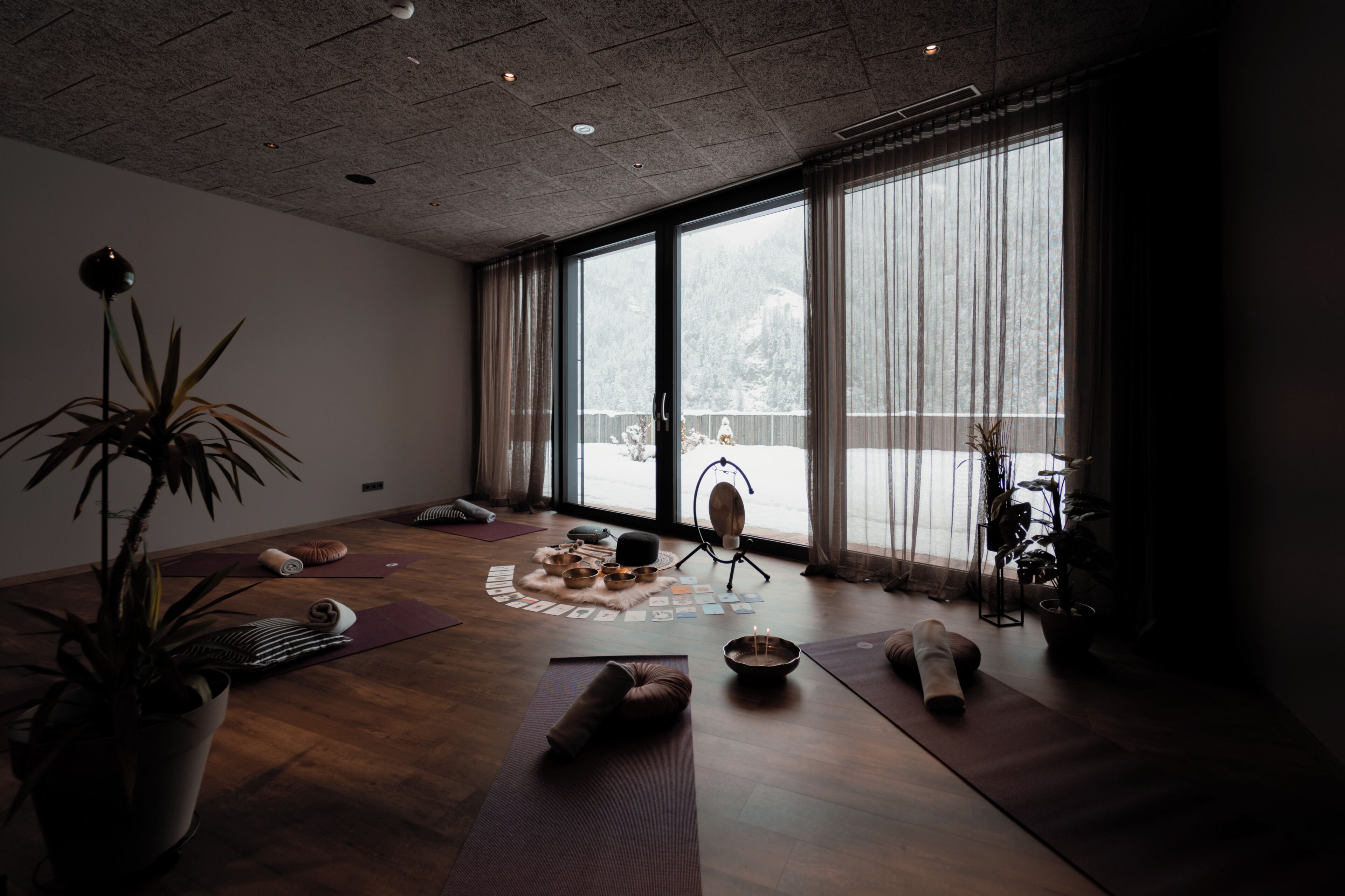 Ein geräumiger Raum mit großen Fenstern, Yogamatten, einer Meditationsgegend und einem Blumentopf.
