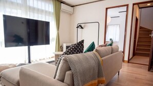 A living room with a sofa, a television, a lamp, and a staircase. - Station Home Lavender (Furano)