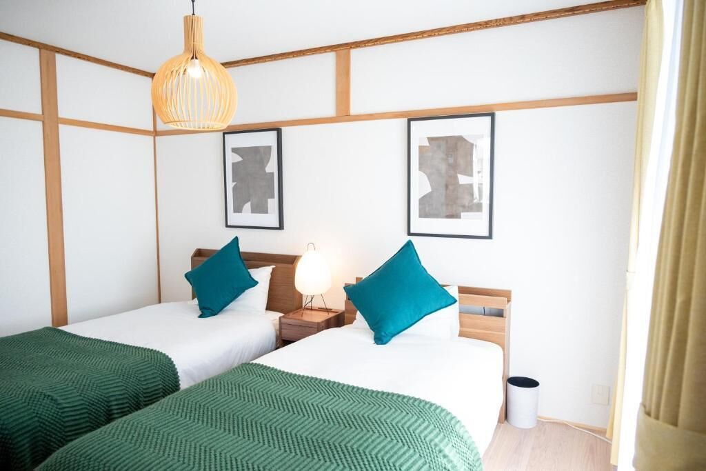 Ein Hotelzimmer mit zwei Betten, grüner Bettwäsche, einem hölzernen Kopfteil, einer Pendelleuchte und zwei gerahmten Bildern an der Wand.