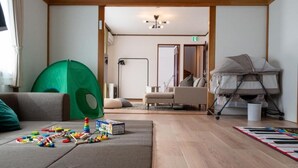 A modern living room with a sofa, a green tent, a baby stroller, and a piano keyboard rug. - Station Home Lavender (Furano)