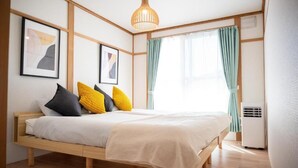 A bedroom with a wooden bed, a ceiling light, and a window with curtains. - Station Home Lavender (Furano)