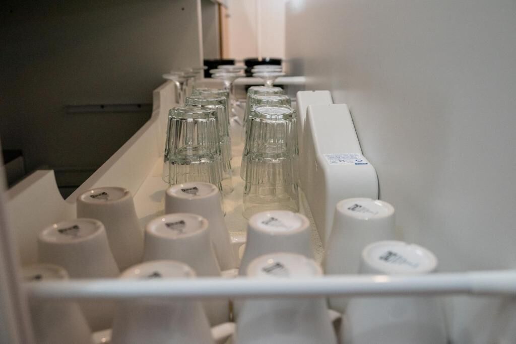 A conveyor belt with glassware and white containers, likely part of a hotel's service area.