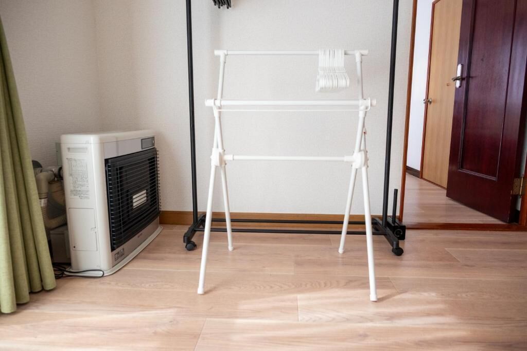 A room with a white drying rack, a standing heater, and a wooden door.