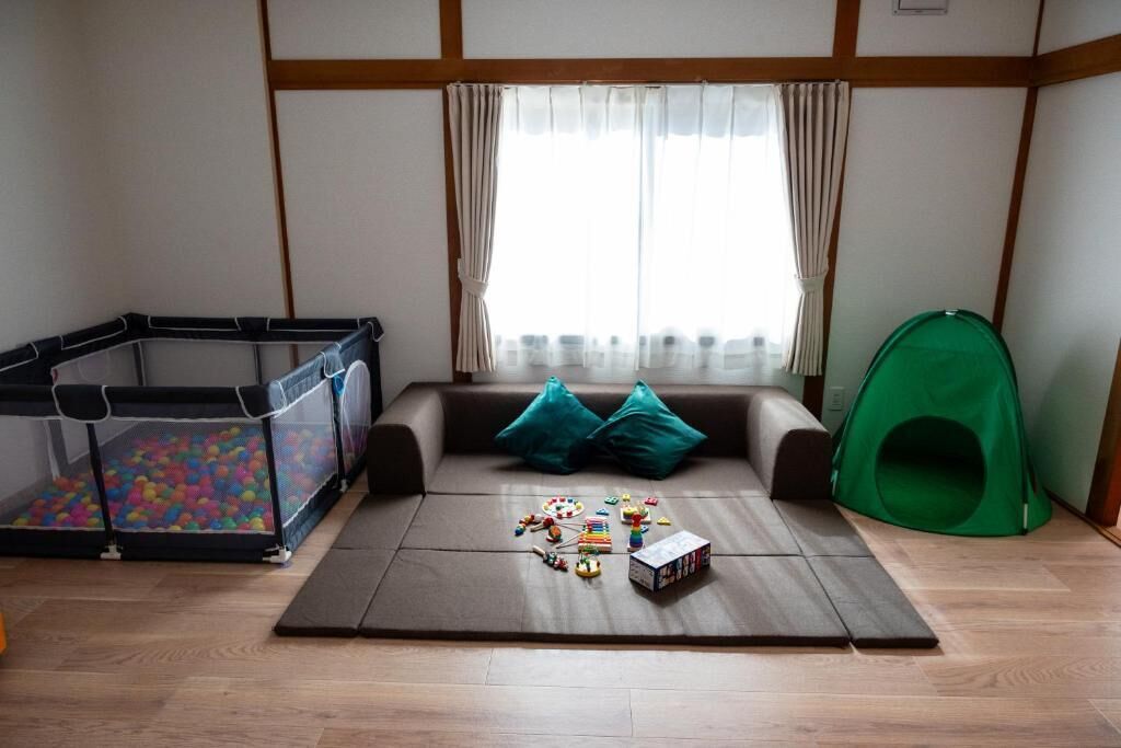A room with a playpen, a green tent, and a play mat with toys.