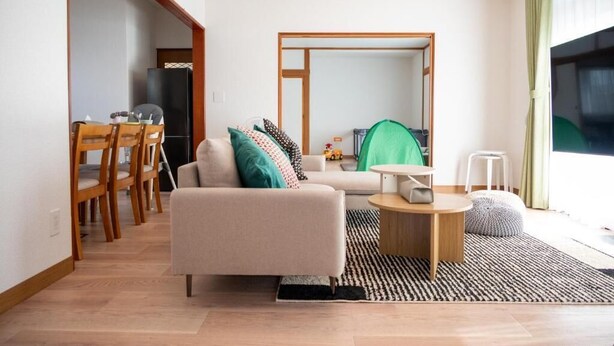 A modern living room with a sofa, coffee table, and a dining area with chairs. - Station Home Lavender (Furano)