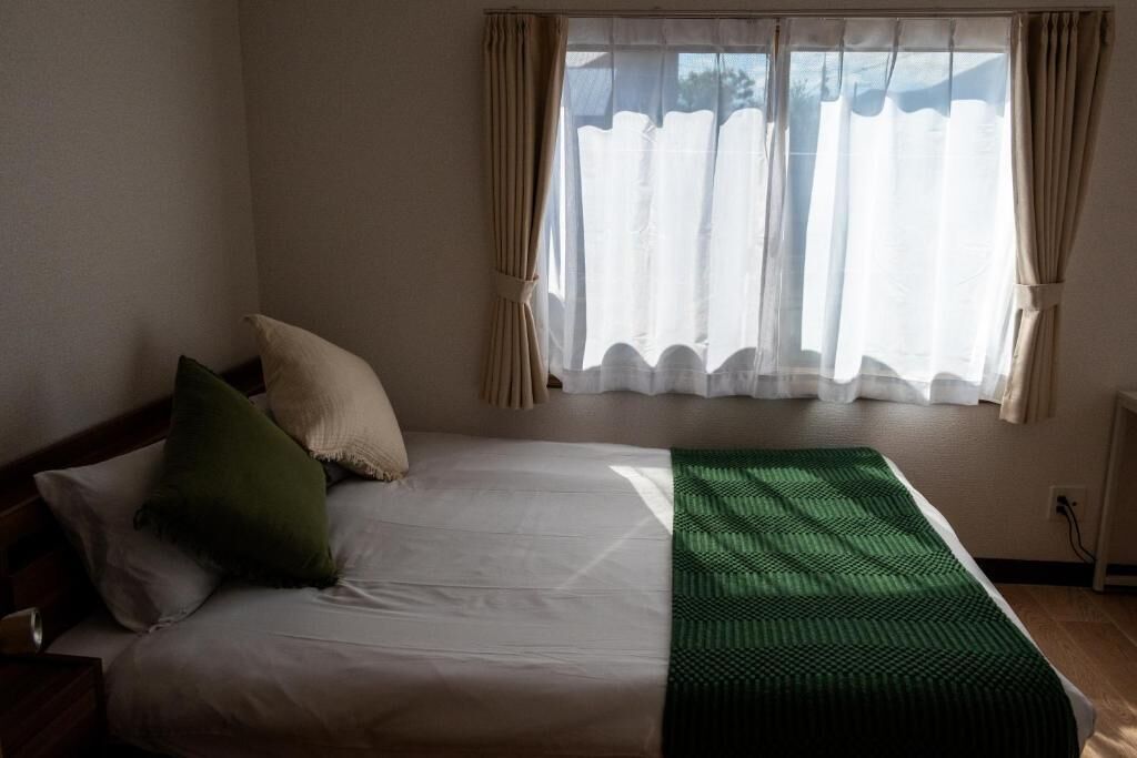 A bedroom with a bed, pillows, a green blanket, and a window with curtains.