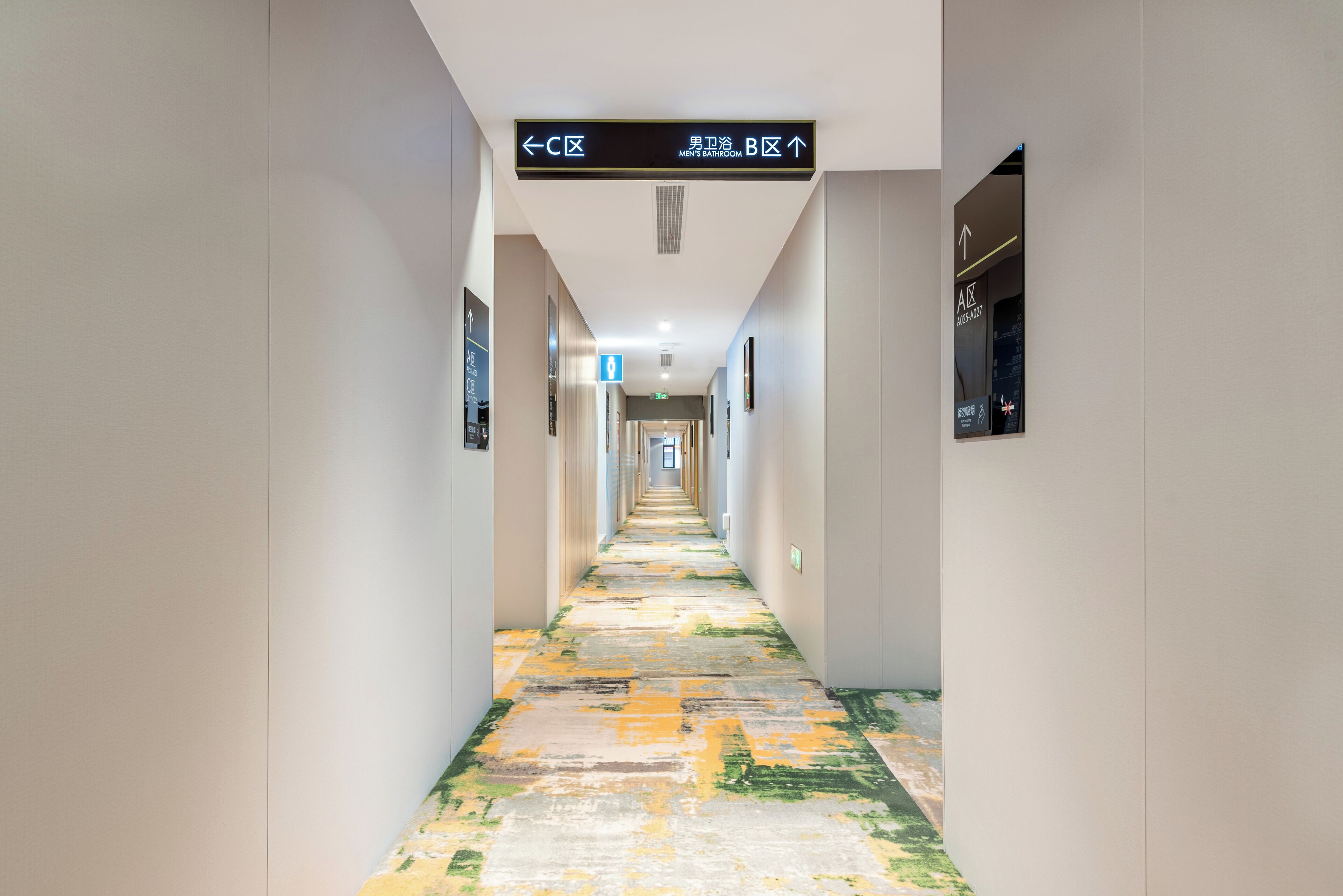 A hotel hallway with directional signs for high and low bathrooms, a blue exit sign, and a patterned floor.