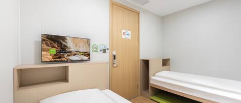 A modern hotel room with a bed, a TV mounted on the wall, a wooden door, and a small shelf.
