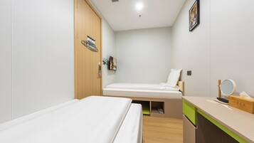 Habitación de hotel pequeña con dos camas individuales, un armario de madera, un escritorio con espejo y un estante con artículos de aseo.