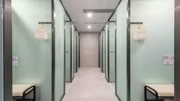A corridor with glass partitions and metal railings, leading to individual rooms.