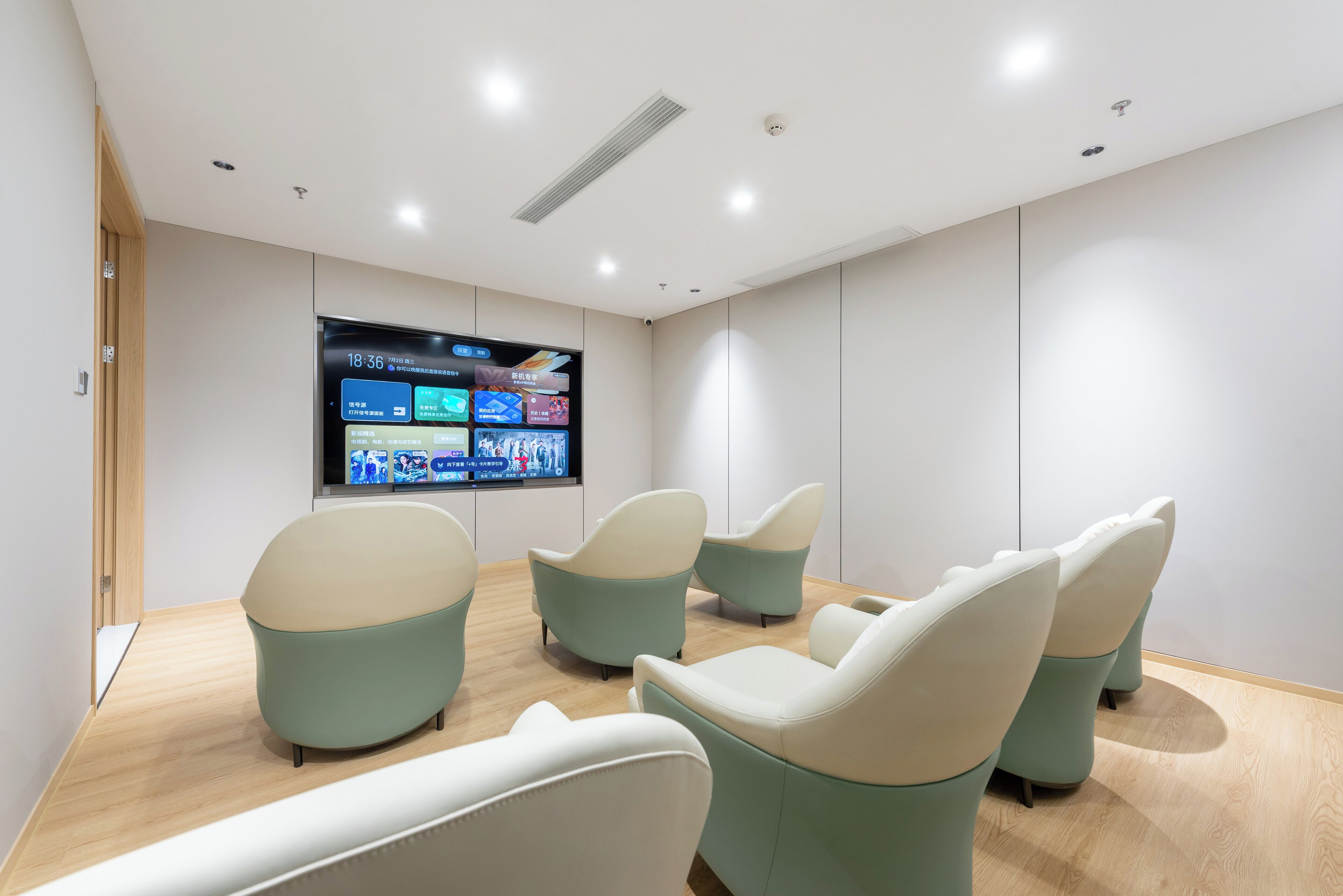 A modern waiting area with a flat-screen TV displaying a schedule, several cushioned chairs, and a wooden floor.