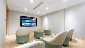 A modern waiting area with a flat-screen TV displaying a schedule, several cushioned chairs, and a wooden floor.