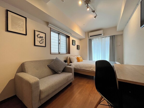 A compact hotel room with a sofa, a bed, a desk, and a chair. - Dash Living Shinjuku (Tokyo)