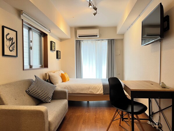 A hotel room with a bed, a desk, a chair, a TV, and an air conditioning unit.