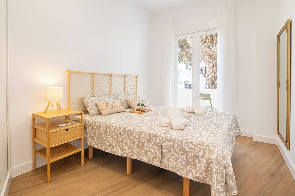 A bedroom with a bed, a bedside table with a lamp, and a window with curtains.