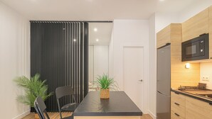 A modern kitchen with a black countertop, wooden cabinets, a stainless steel refrigerator, and a microwave. There is a dining table with chairs and a potted plant. - Calahonda Beach (Mijas)