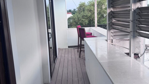 Un couloir étroit, doté d’un plancher en bois, mène à un balcon agrémenté d’une rambarde en métal et d’une chaise.