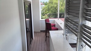 Un balcon étroit doté d’un plancher en bois, d’une chaise rouge et d’une balustrade blanche.