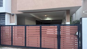 Une entrée fermée par un portail mène à un bâtiment doté d’un toit plat et de murs extérieurs de couleur claire.