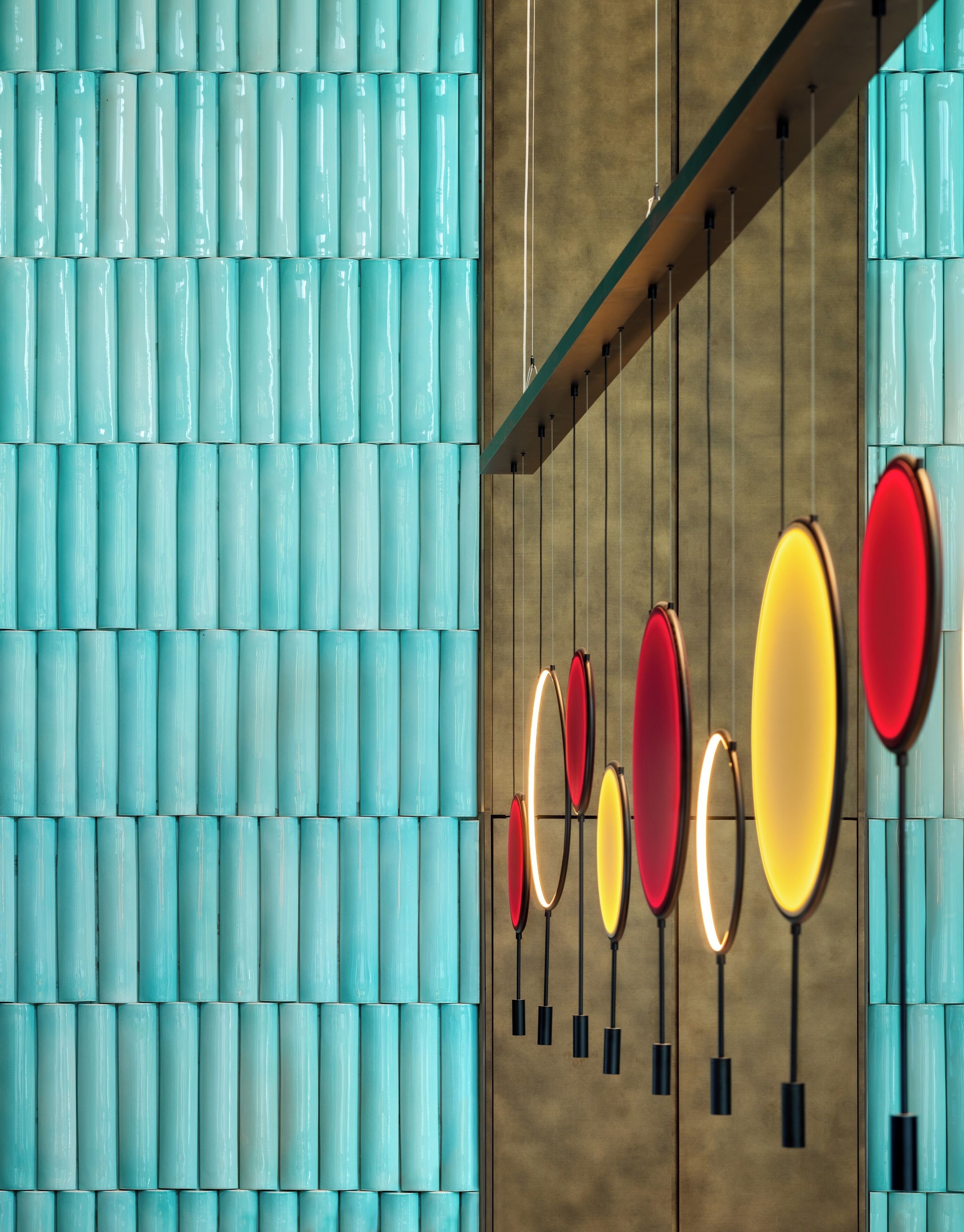 A wall with a pattern of teal cylindrical shapes and a series of oval-shaped light fixtures in red, yellow, and white colors.