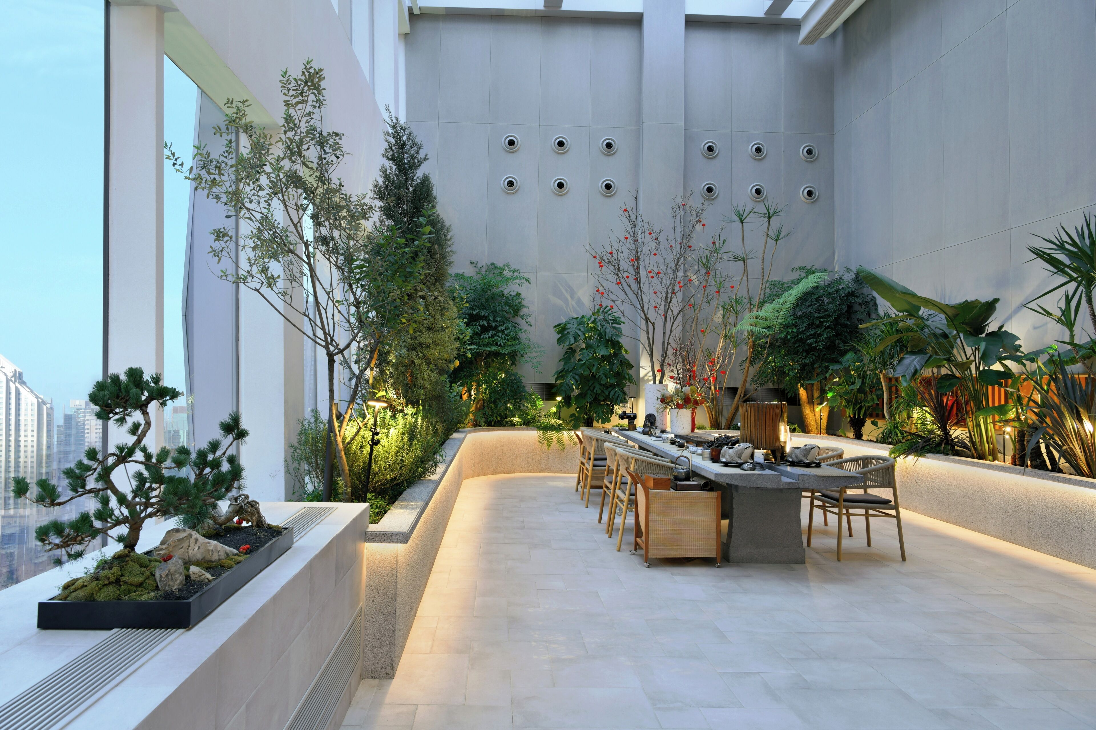 A modern indoor garden with a seating area, plants, and a view of the city.
