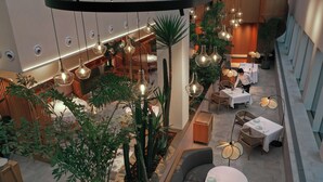 Un espacio interior moderno con varias zonas de comedor, lámparas colgantes y abundante vegetación de interior.