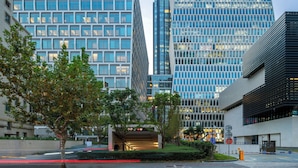 Una calle urbana moderna con edificios altos, incluyendo un rascacielos con una curva distintiva y un edificio con fachada de entramado.
