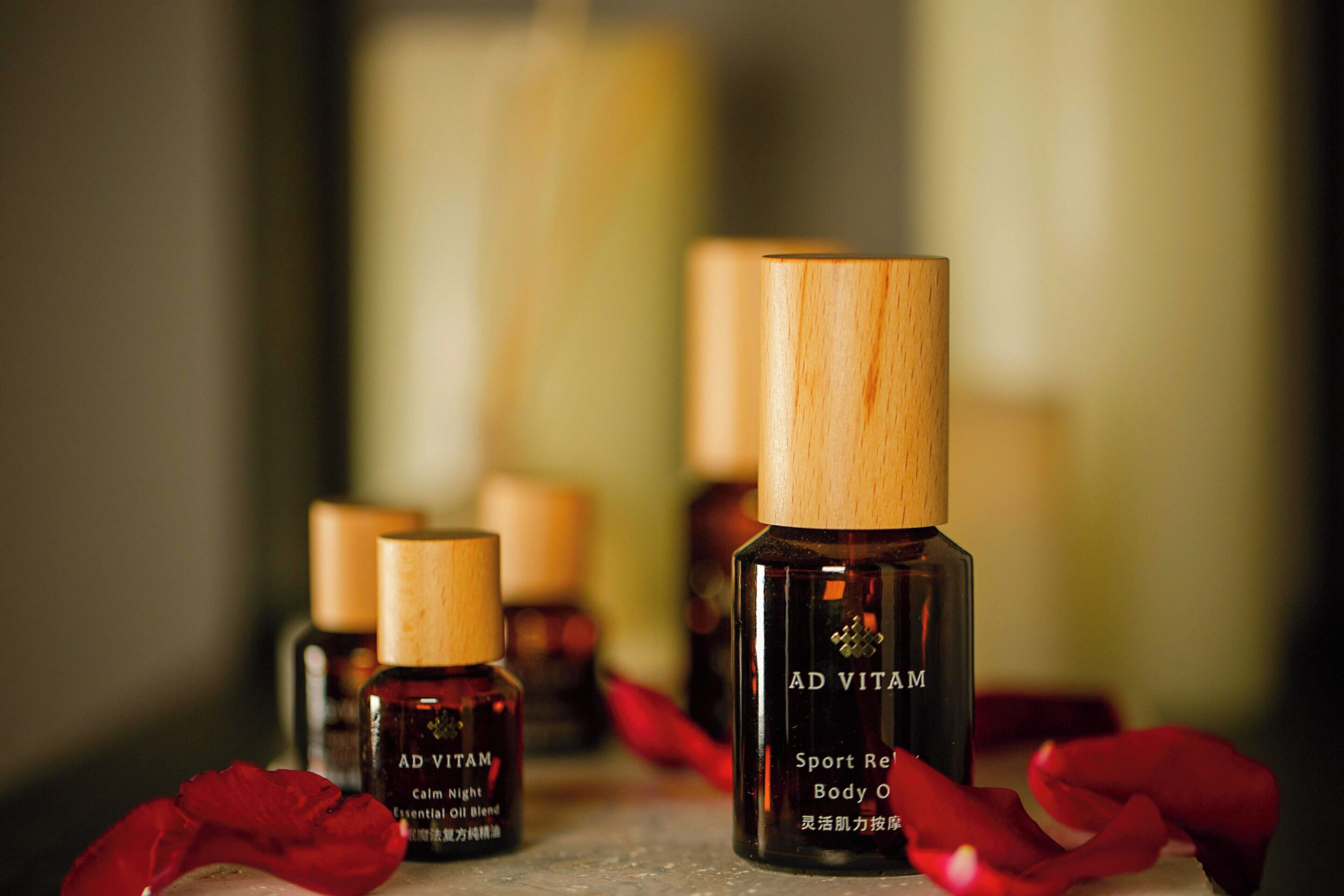 Several bottles of Ad Vital Sport Relief Body Oil with wooden caps, arranged on a surface with red rose petals.