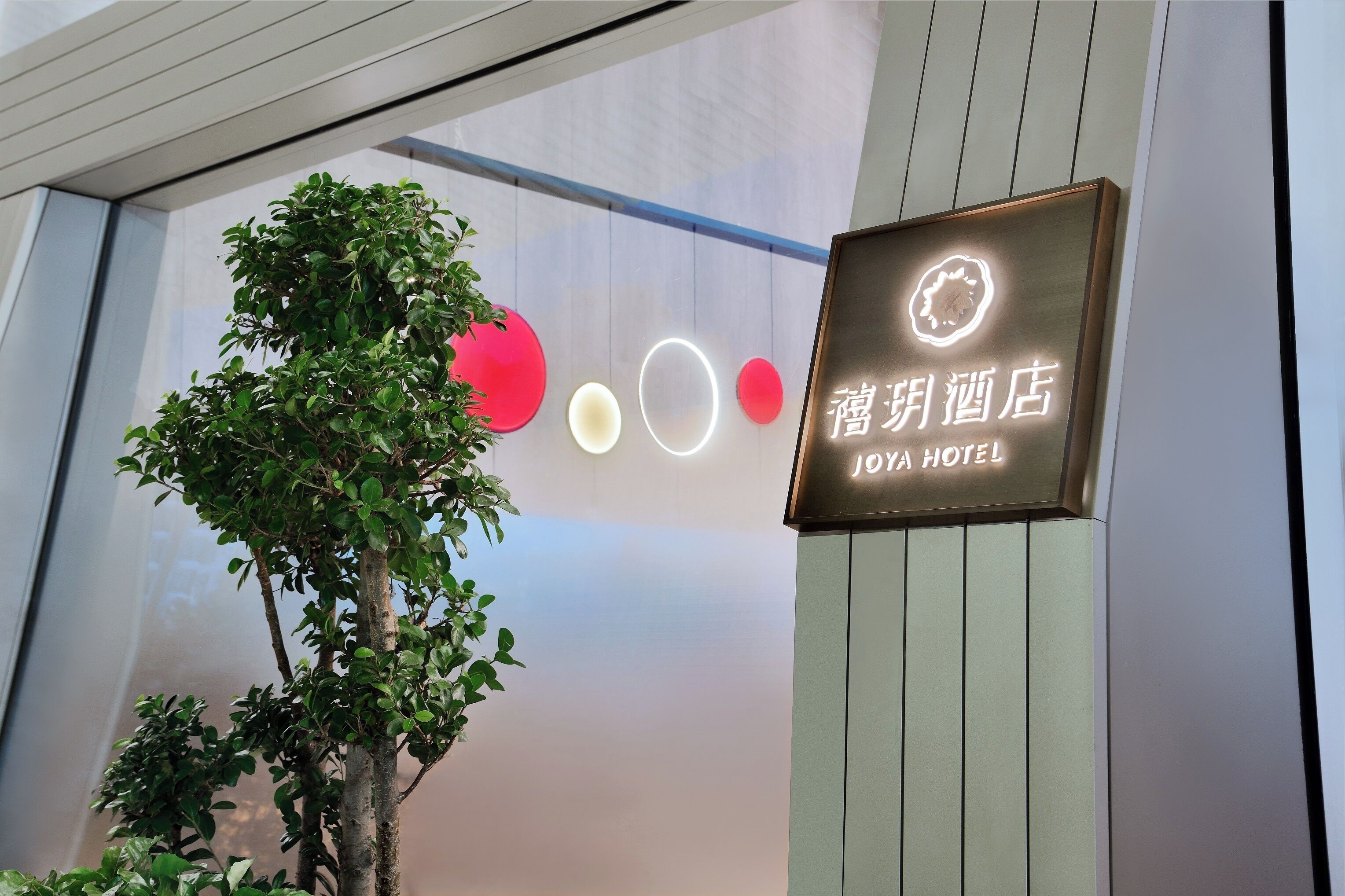 A hotel sign with illuminated circles and a tree in front.